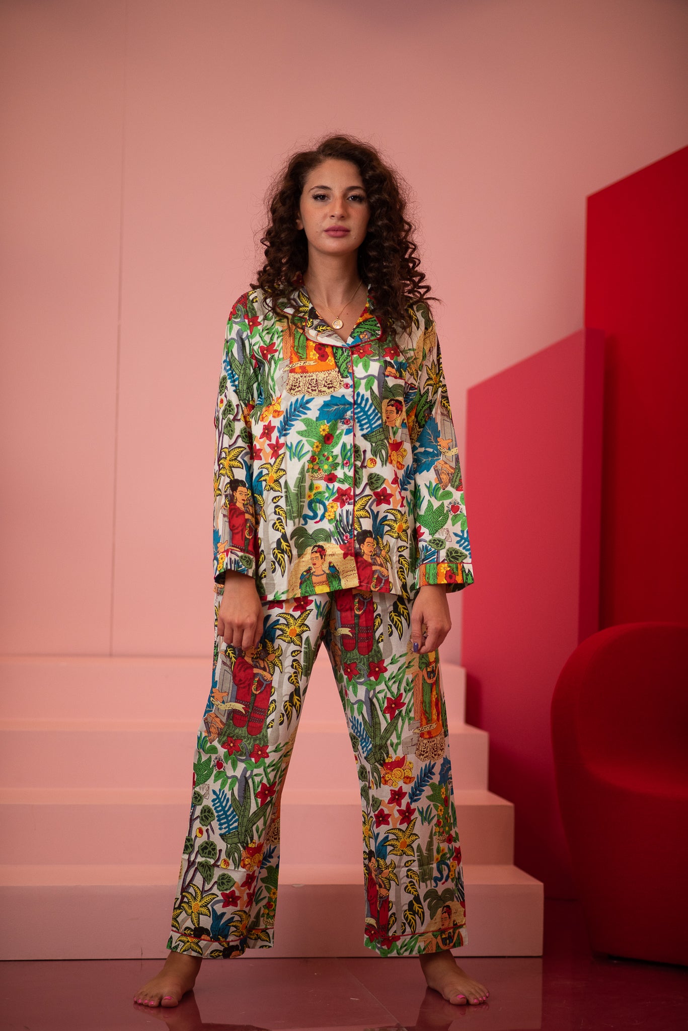 Woman wearing a colorful patterned outfit standing in a pink room with red accents.